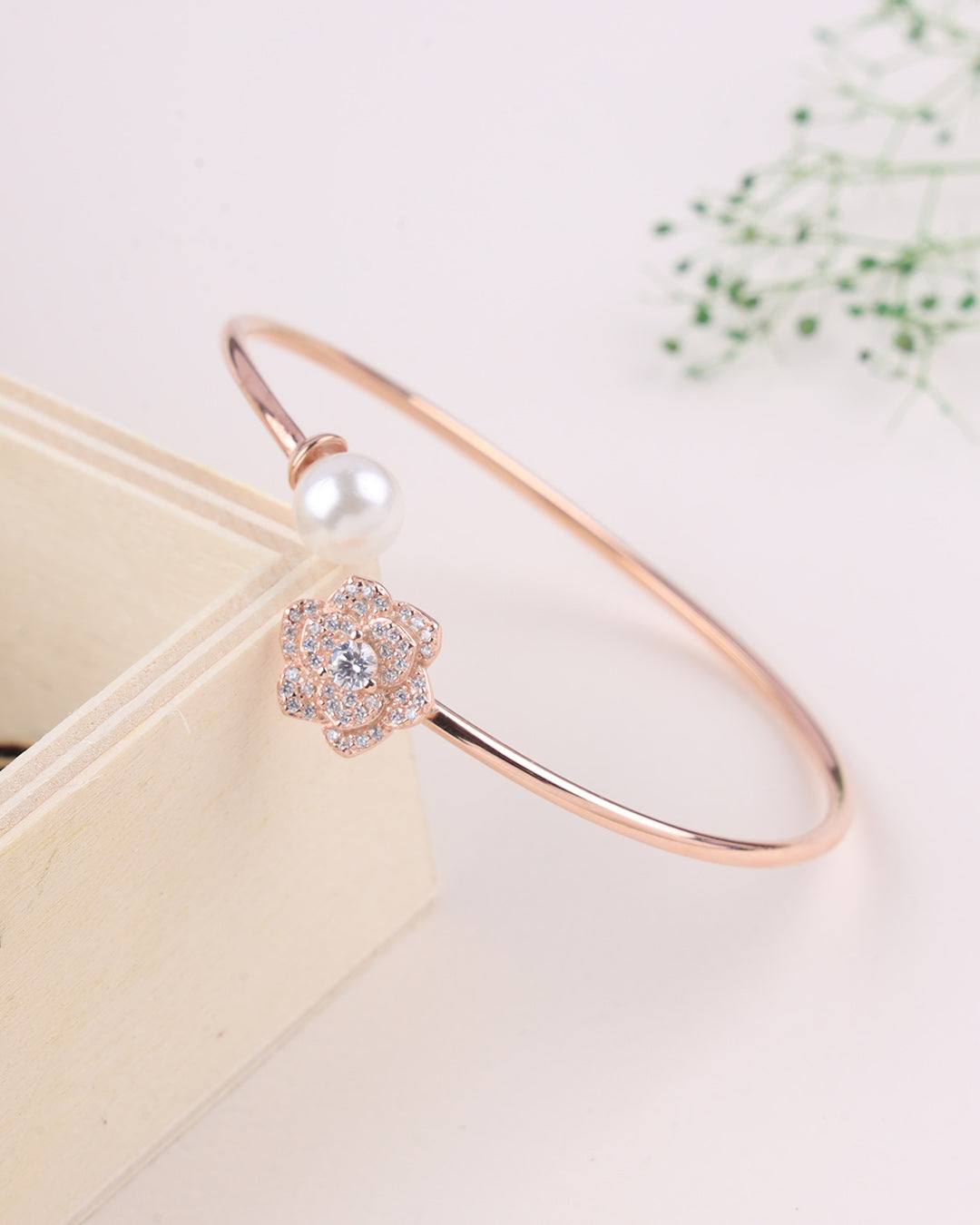 Rose gold bracelet with a floral clasp and pearl on a light background