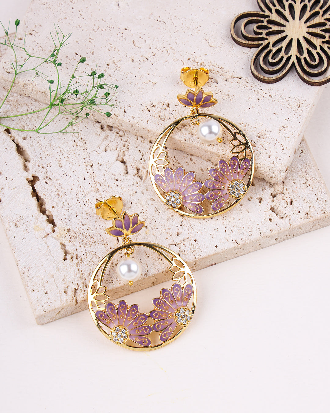 Pair of gold and purple floral earrings on a textured surface with greenery.