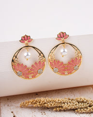 Ornate earrings with pink floral designs and pearls on a textured surface.