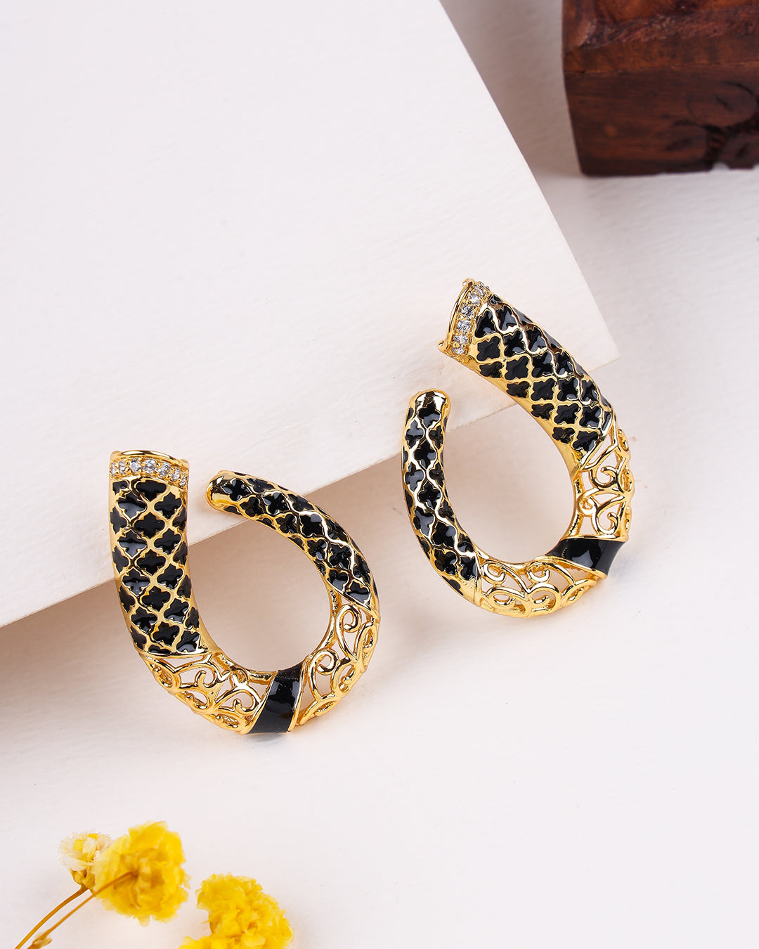 Gold and black hoop earrings on a light background with yellow flowers.