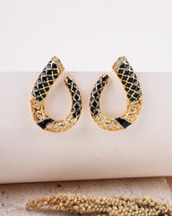 Gold and black hoop earrings on a white surface with a natural element in the background