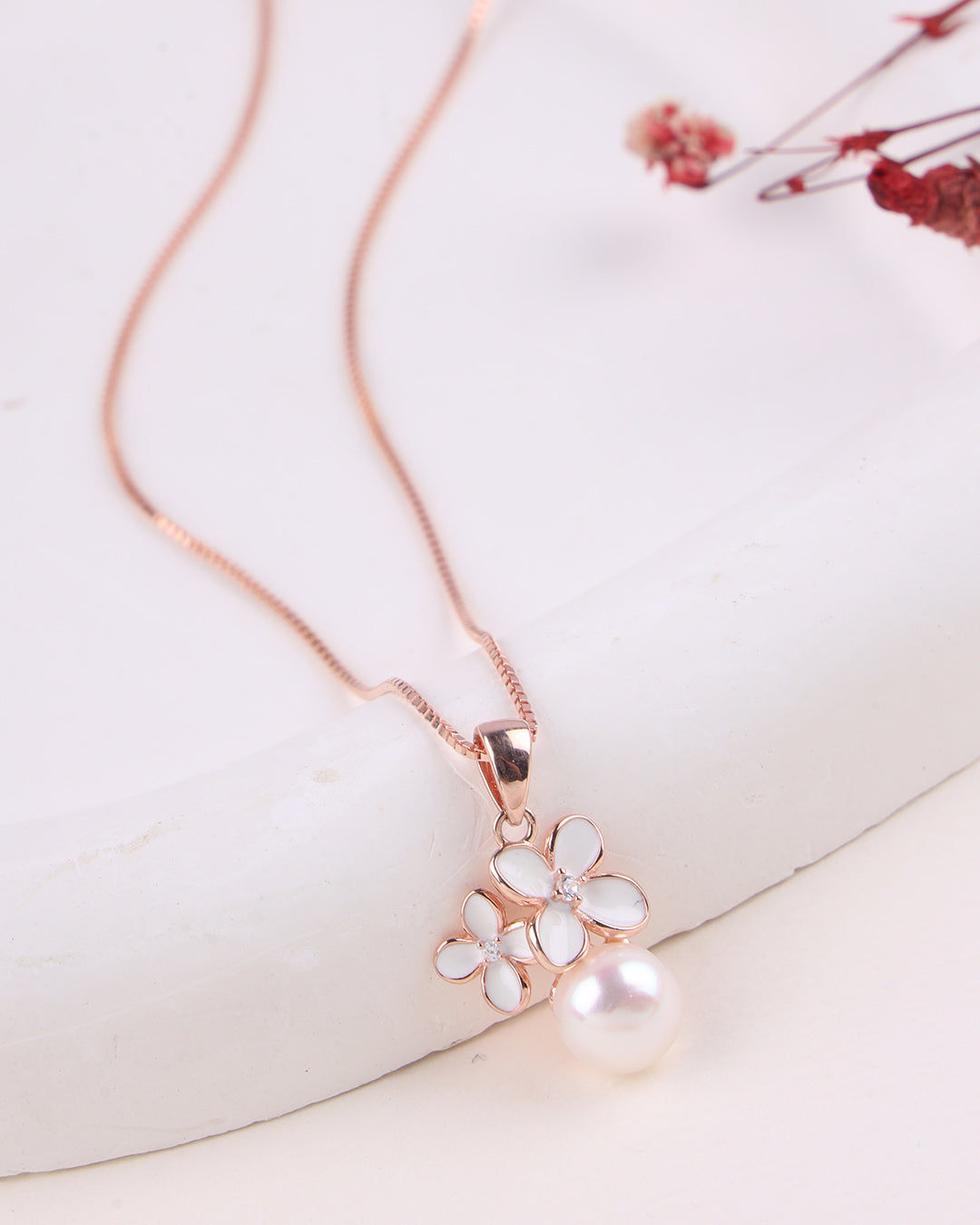 Pearl necklace with rose gold chain on a white surface