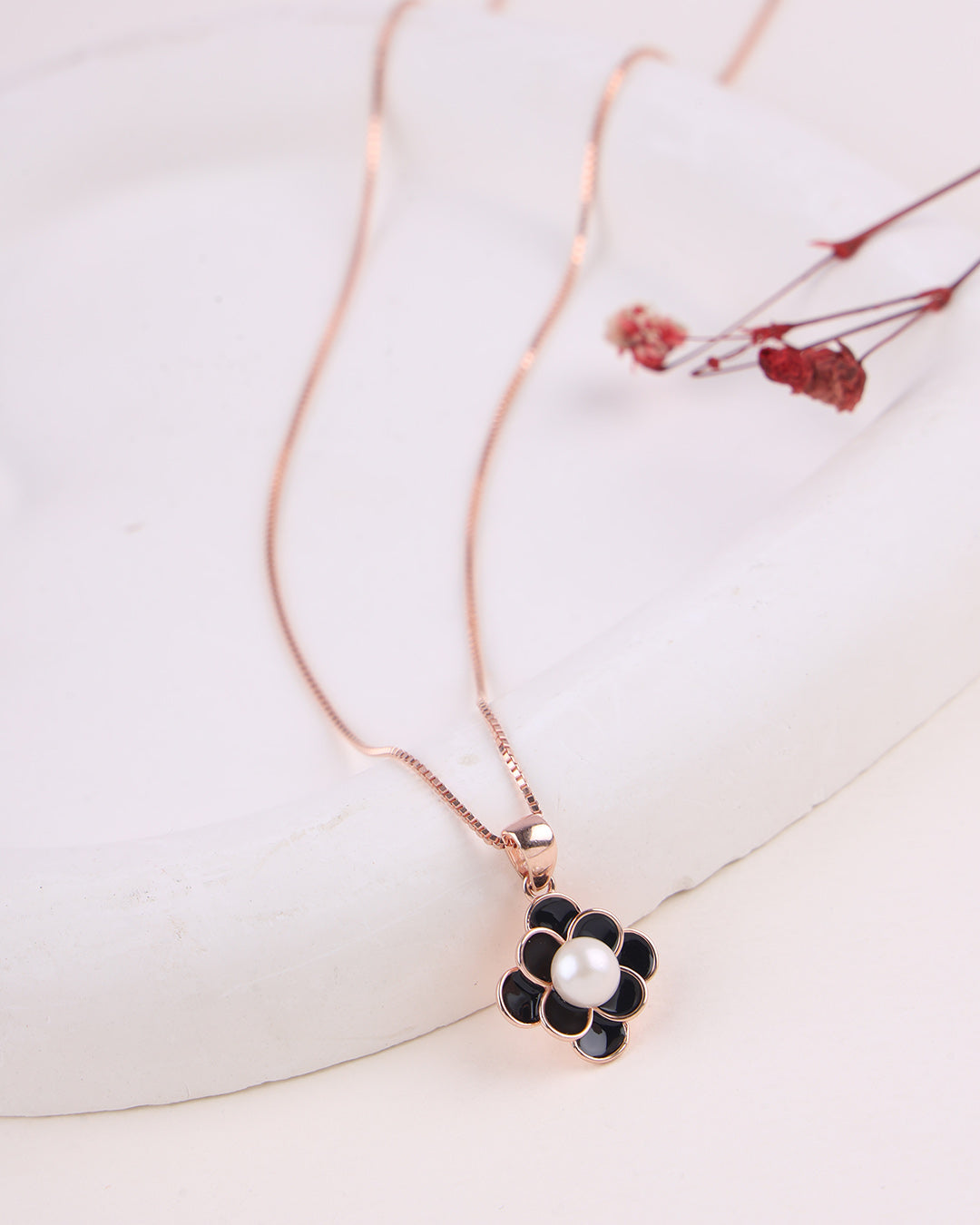 Rose gold necklace with a black flower pendant on a white surface