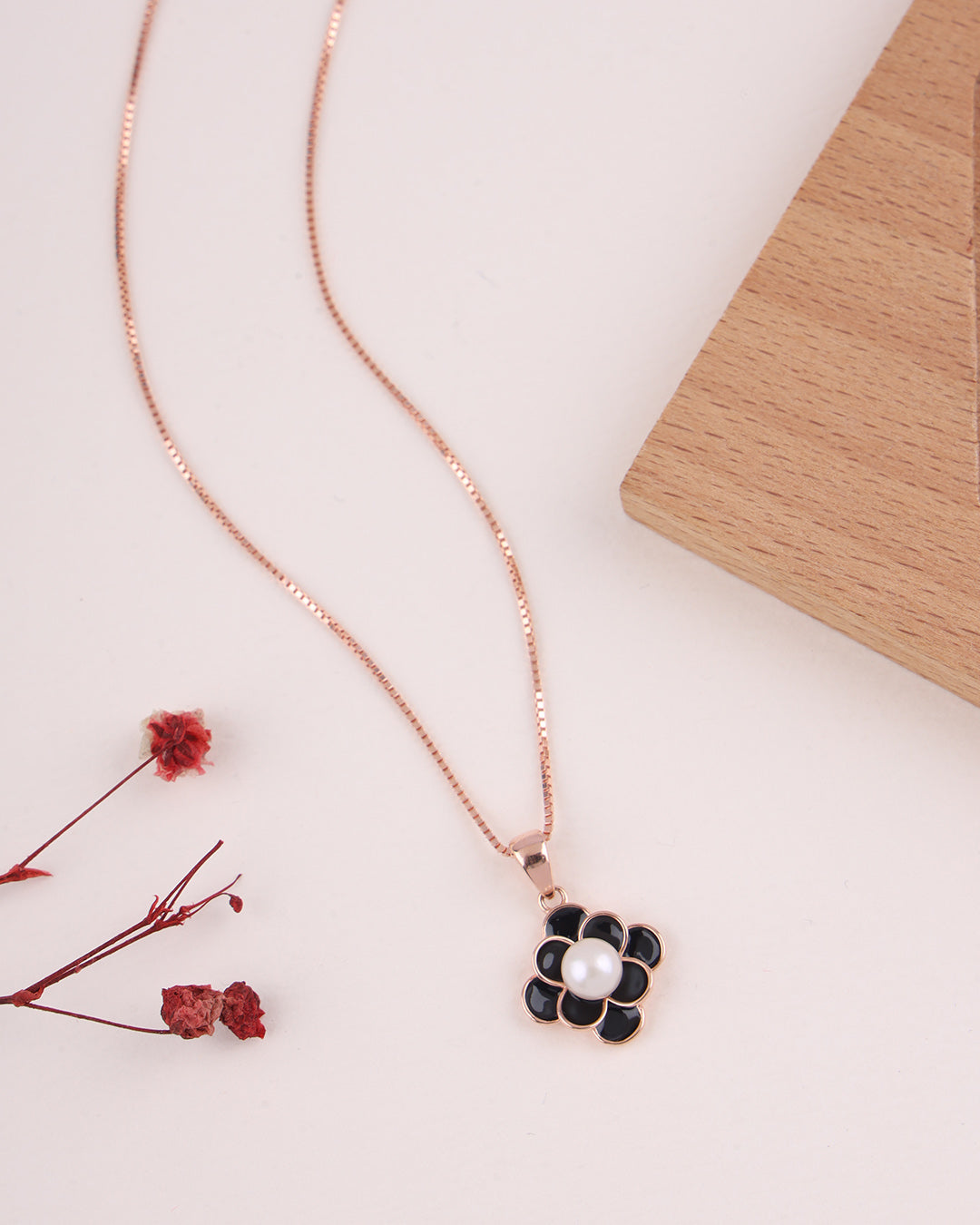 Necklace with a floral pendant on a light surface with dried flowers.