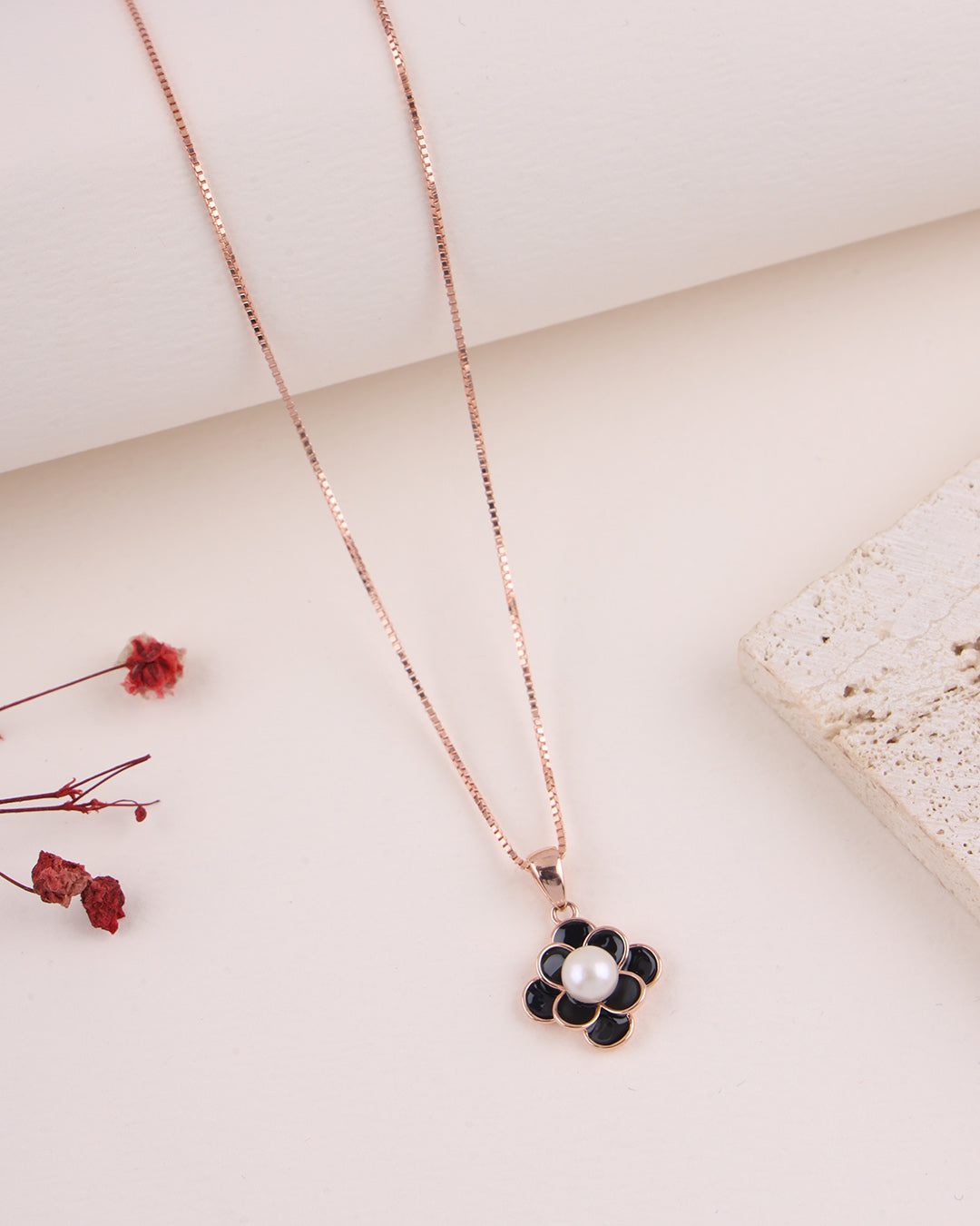 Rose gold necklace with a black floral pendant on a light background