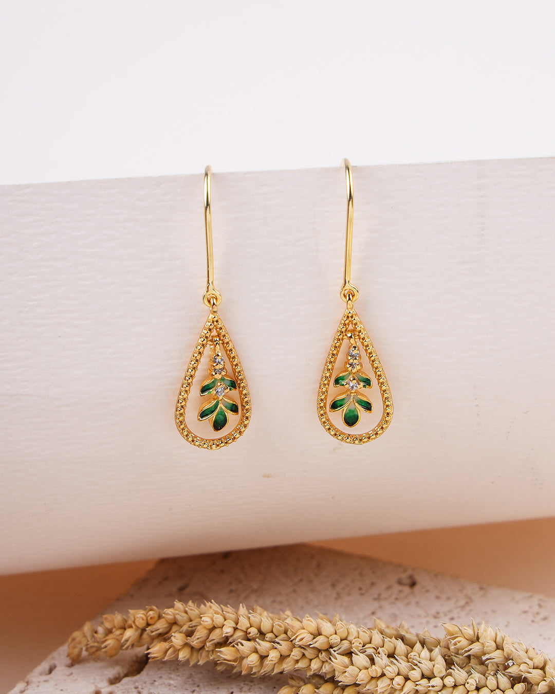 Gold earrings with green gemstones on a white surface