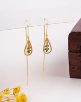 Gold teardrop earrings with green stones on a white background