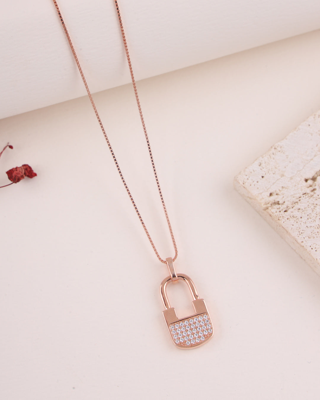 Rose gold padlock-shaped necklace with clear stones on a light background