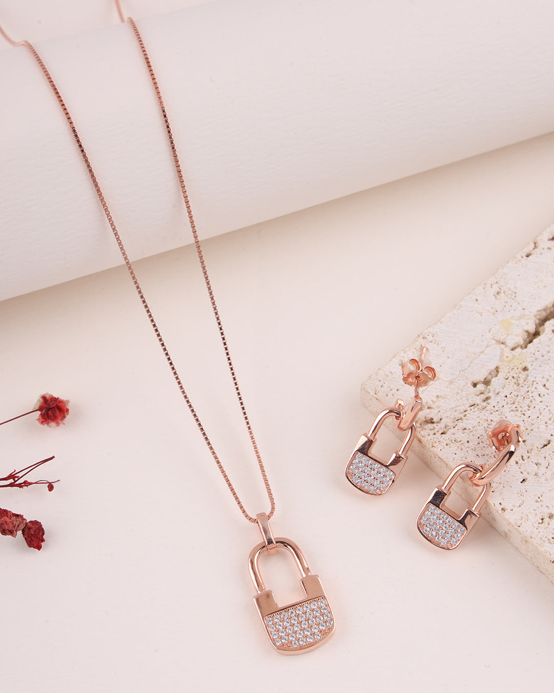 Rose gold lock-shaped necklace and earrings on a light background