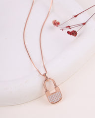 Rose gold padlock-shaped pendant with clear stones on a white surface with dried flowers.