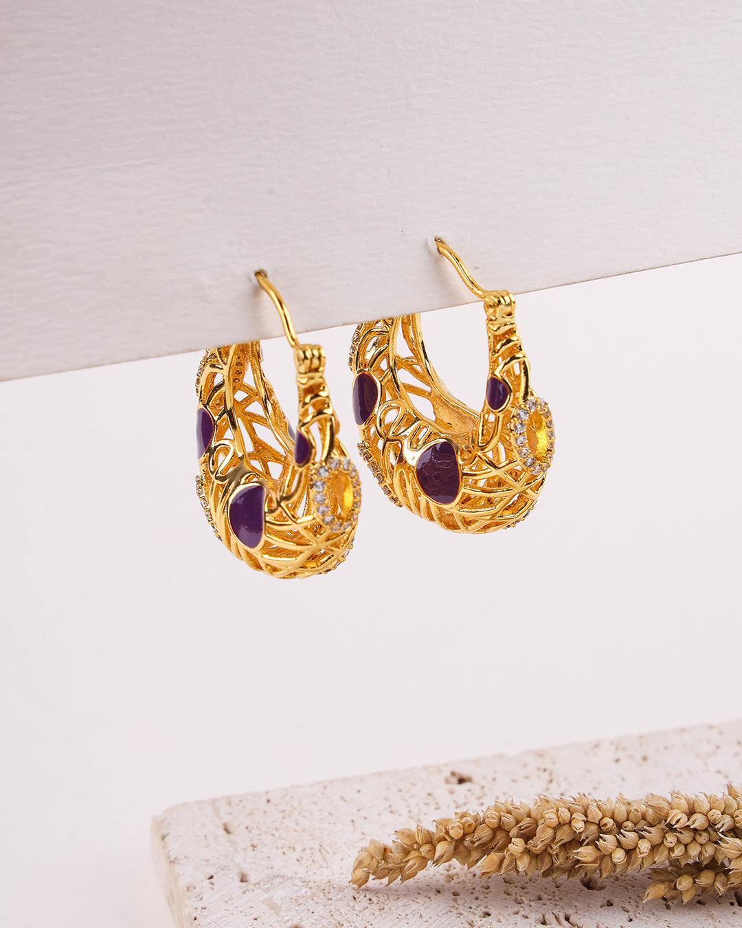 Gold earrings with purple stones on a light background