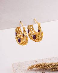Gold earrings with purple stones on a light background