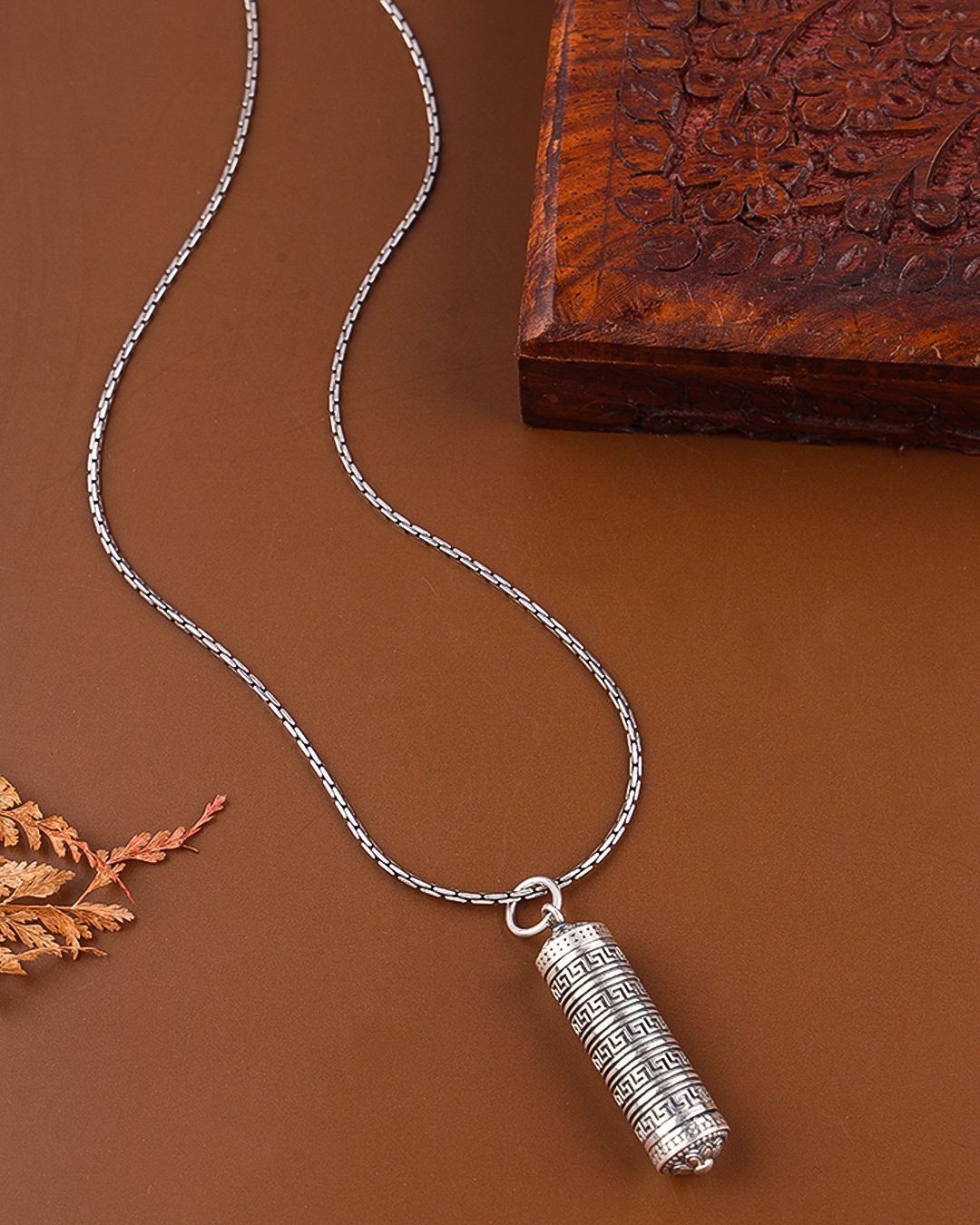 Silver necklace with a cylindrical pendant on a brown background