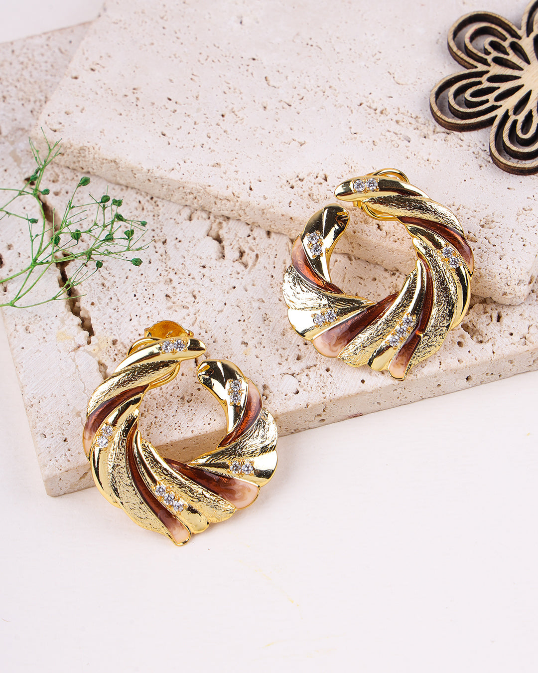 Gold and rose gold earrings on a textured stone surface with a decorative element.