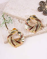 Gold and rose gold earrings on a textured stone surface with a decorative element.
