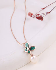 Necklace with a green butterfly pendant and pearl on a light background