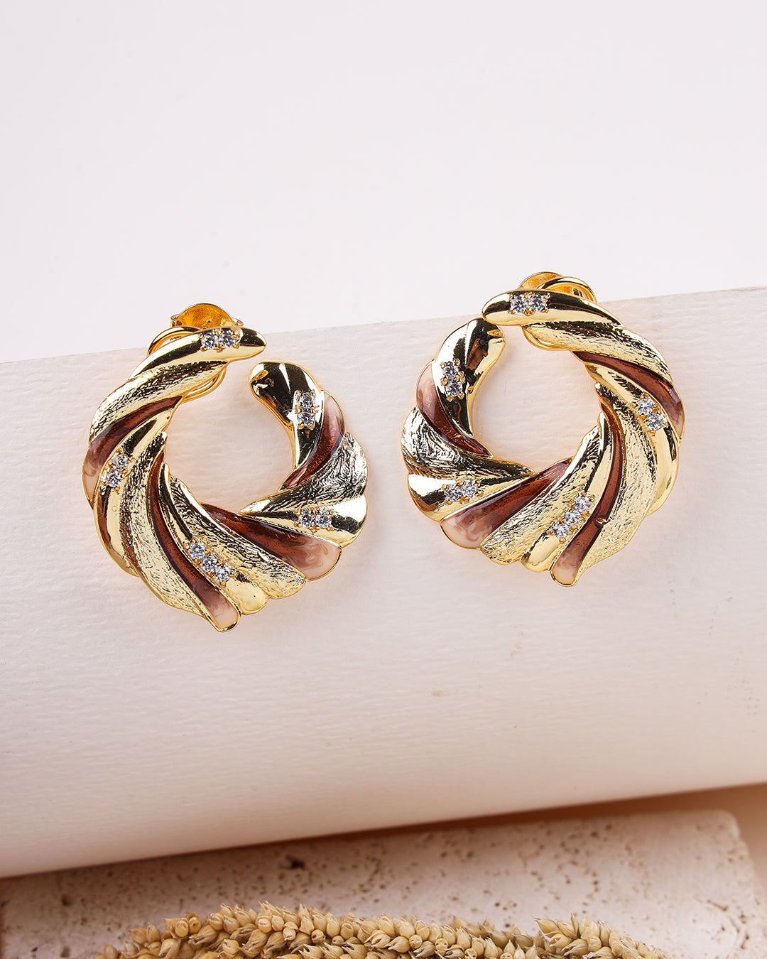Gold hoop earrings with a twisted design on a beige surface.