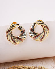 Gold hoop earrings with a twisted design on a beige surface.