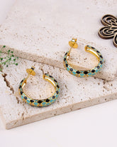 Gold hoop earrings with blue and black enamel on a textured surface
