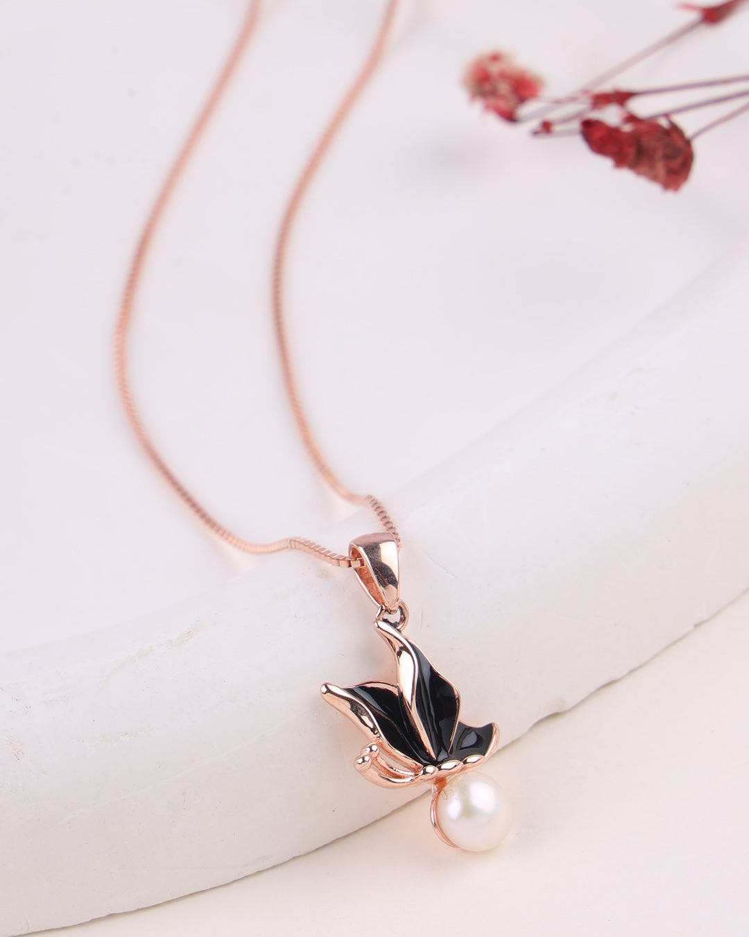 Rose gold necklace with a leaf and pearl pendant on a white background