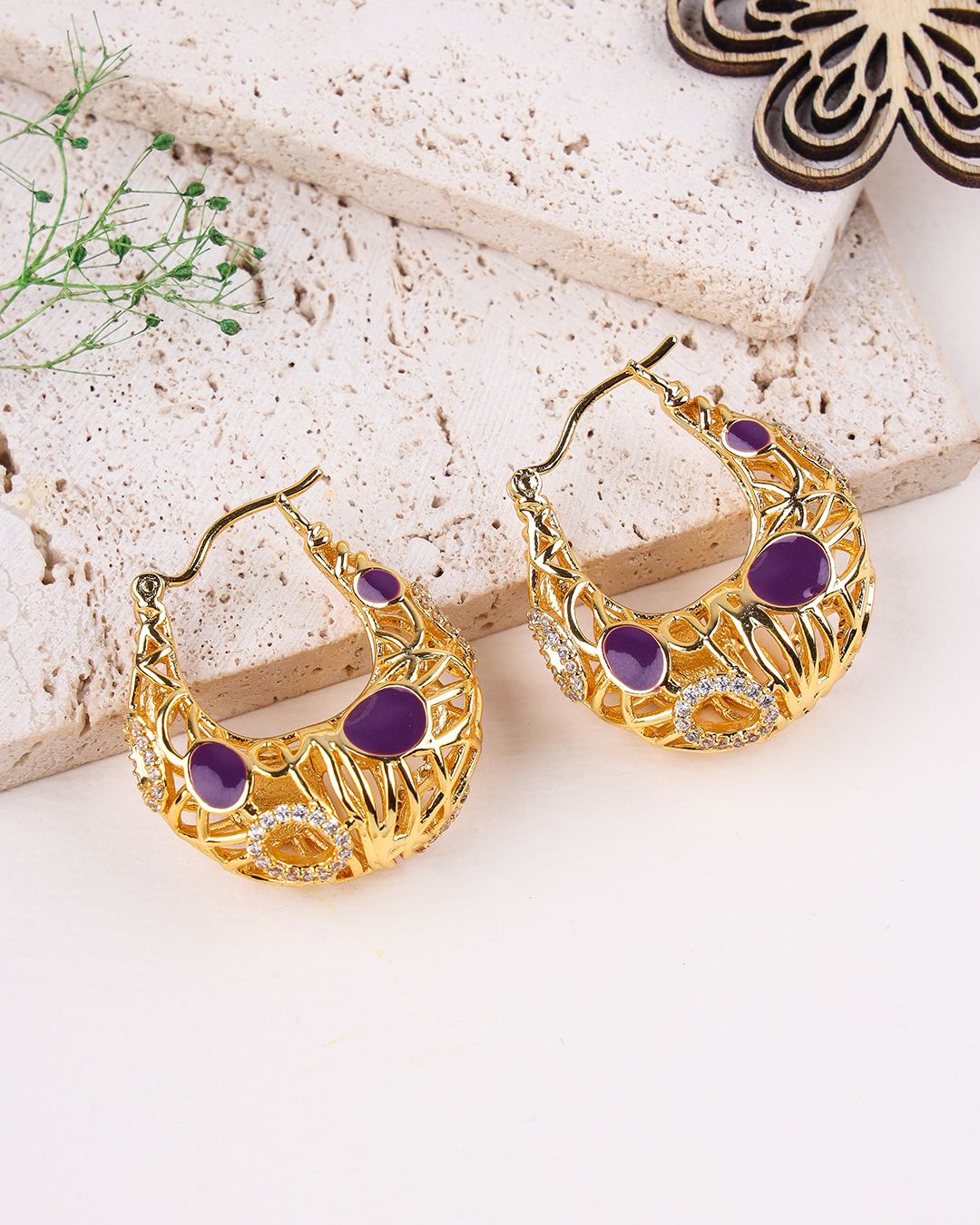 Gold hoop earrings with purple stones on a light background