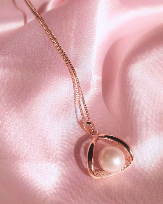 Rose gold necklace with a heart-shaped pendant featuring a pearl on a pink fabric background