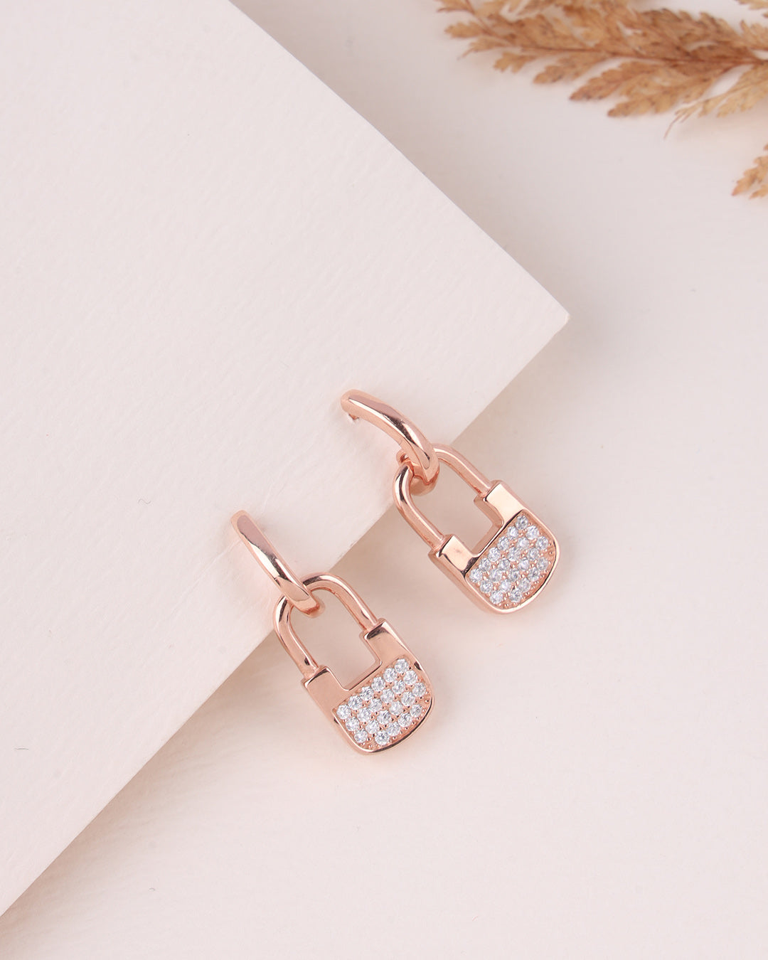 Rose gold lock-shaped earrings with diamond accents on a light background
