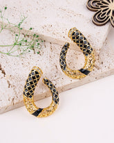 Gold and black hoop earrings on a textured surface with a plant