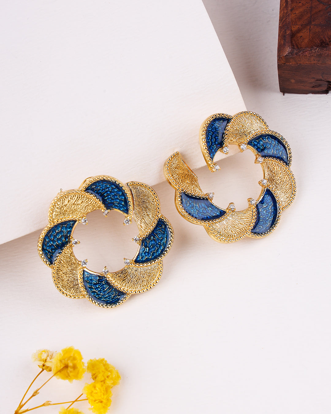 Gold and blue earrings on a white surface with yellow flowers.