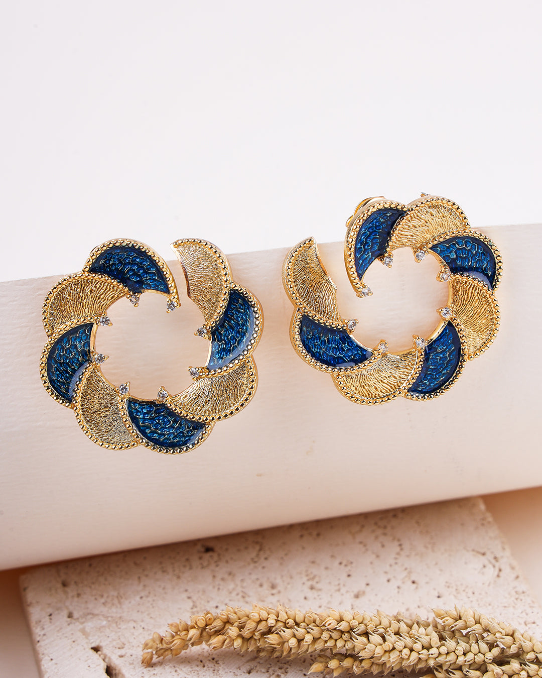Gold and blue earrings on a white surface with a natural background