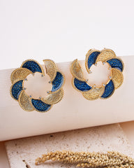 Gold and blue earrings on a white surface with a natural background