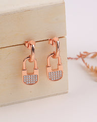 Rose gold lock-shaped earrings with clear gemstones on a wooden box.