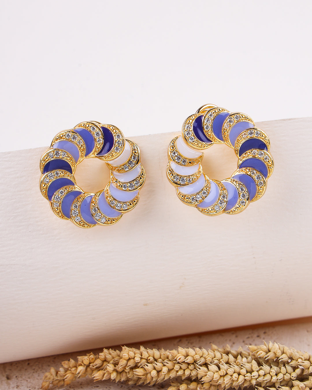 Pair of gold hoop earrings with blue and white circular patterns on a beige surface.