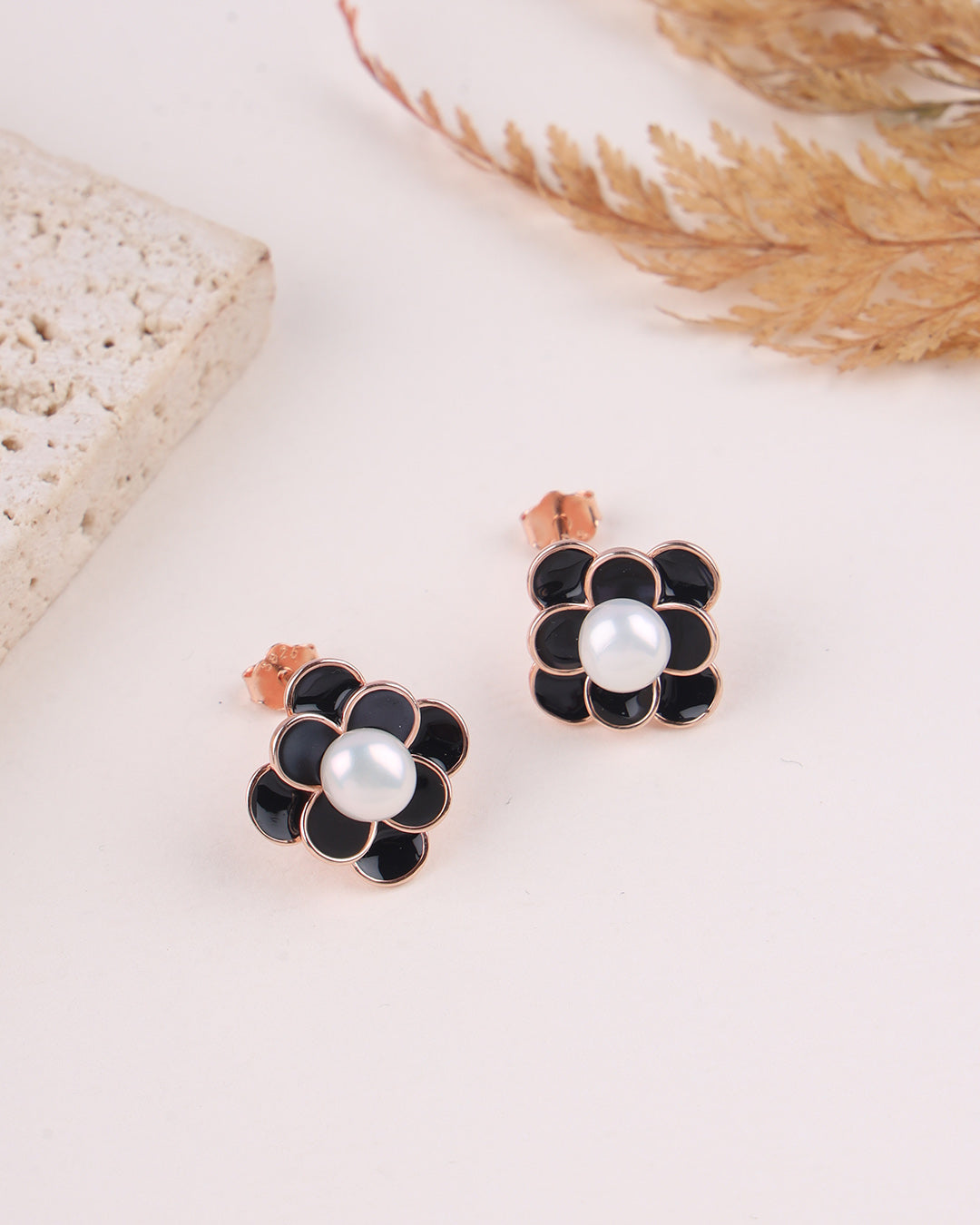 Pair of black flower-shaped earrings with pearl centers on a light surface.