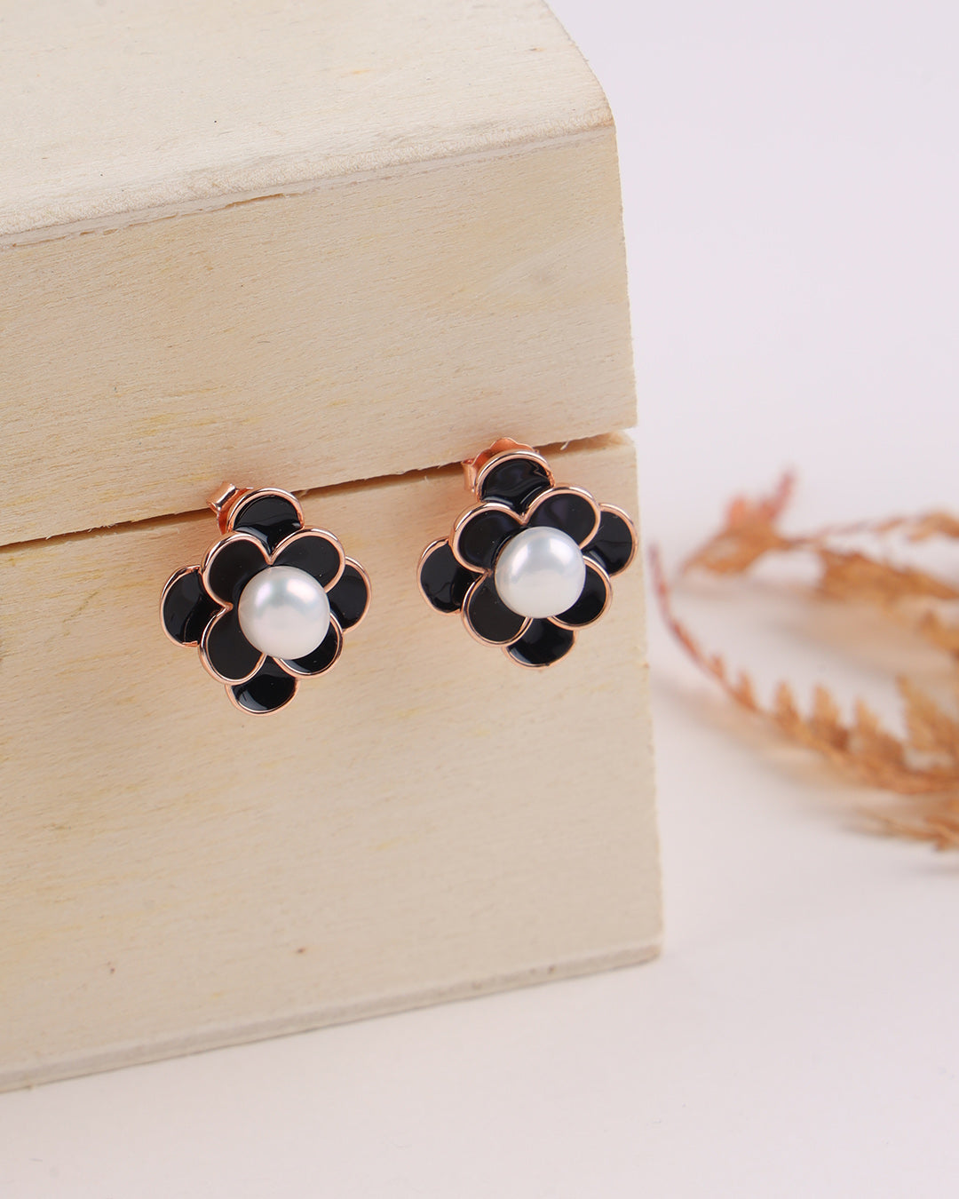 Black flower-shaped earrings with white pearls on a wooden box