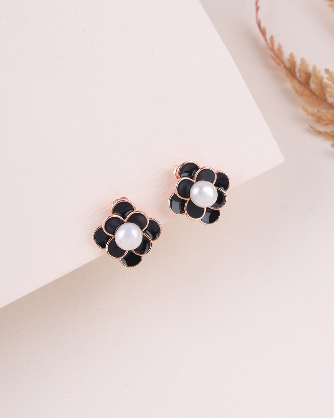 Black flower-shaped earrings with pearl centers on a light beige background