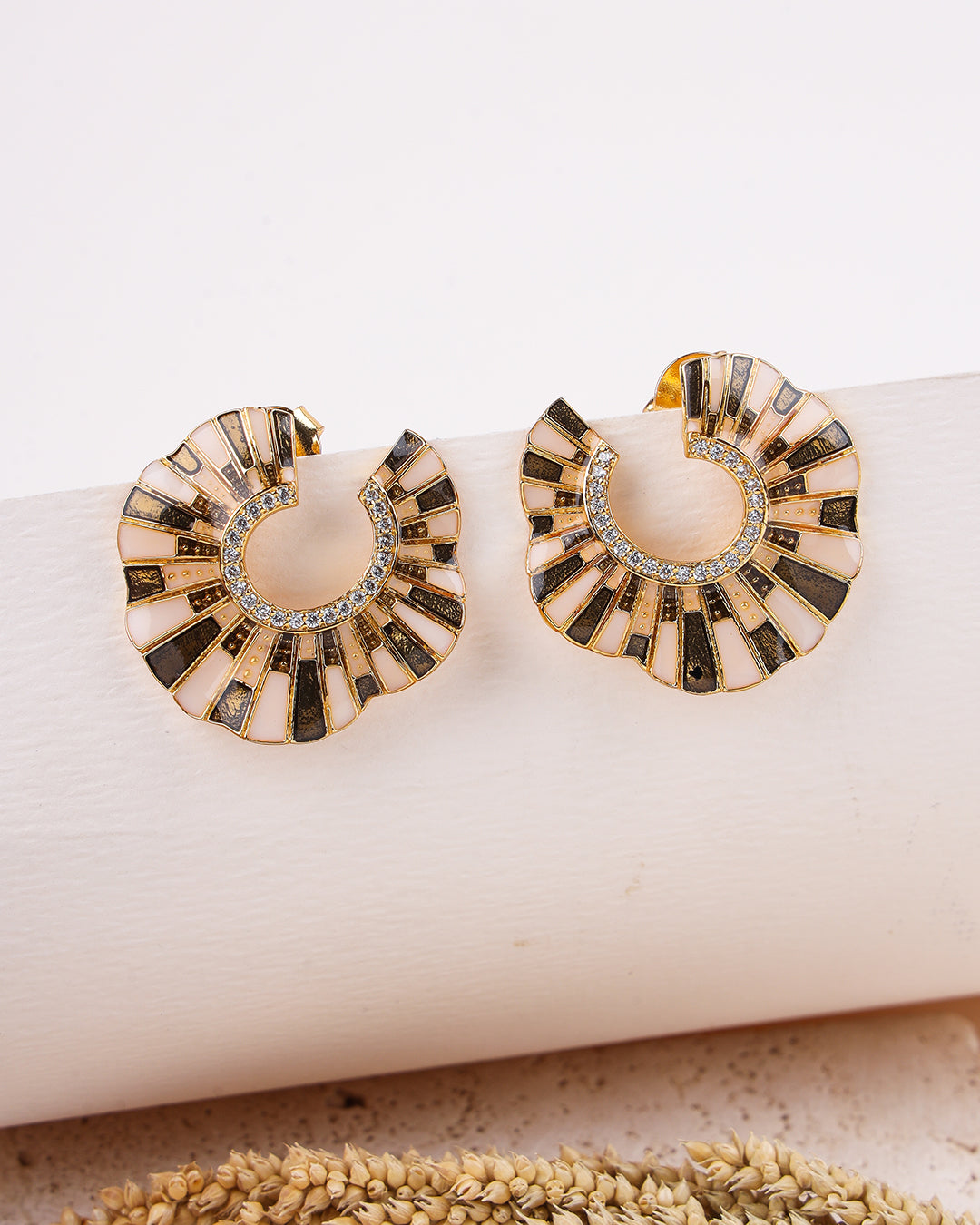 Pair of gold and black earrings on a white surface with a natural background.
