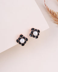 Black flower-shaped earrings with pearl centers on a light beige background