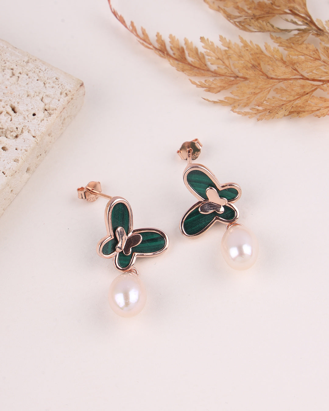 Butterfly-shaped earrings with green accents and pearl drops on a light background
