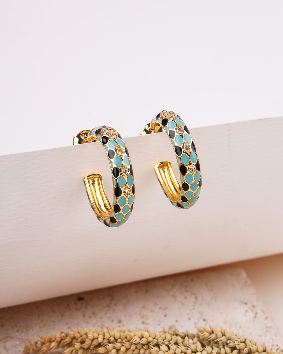 Gold hoop earrings with blue and black pattern on a beige surface