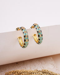 Gold hoop earrings with blue and black pattern on a beige surface