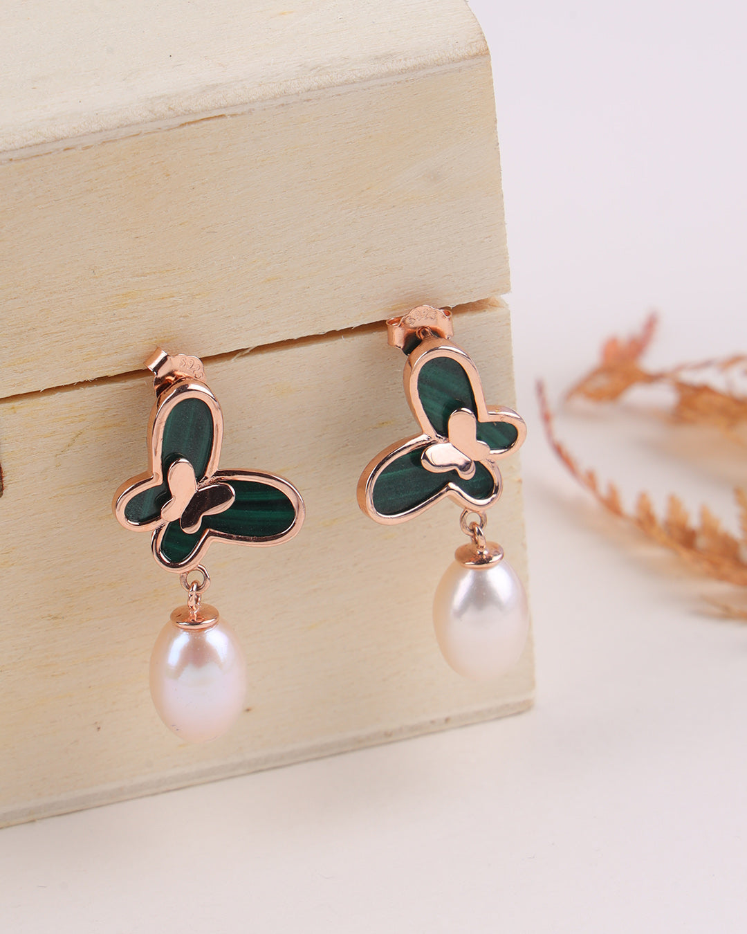 Butterfly-shaped earrings with rose gold and green details on a wooden stand.