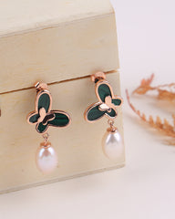 Butterfly-shaped earrings with rose gold and green details on a wooden stand.