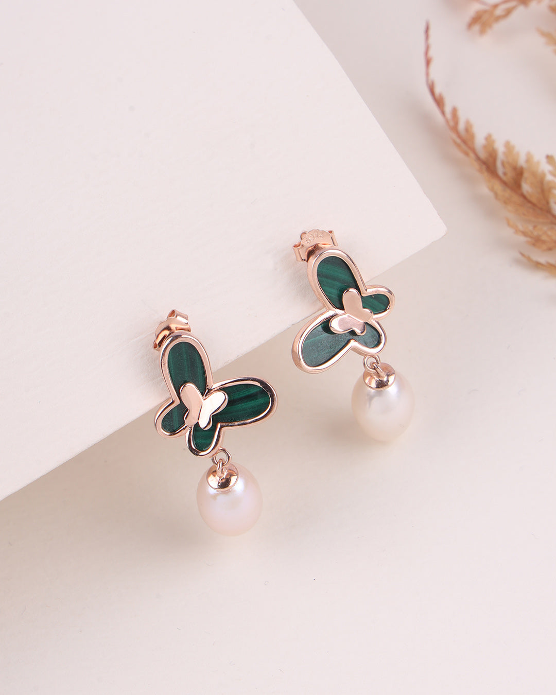 Butterfly-shaped earrings with green wings and pearl drops on a light background