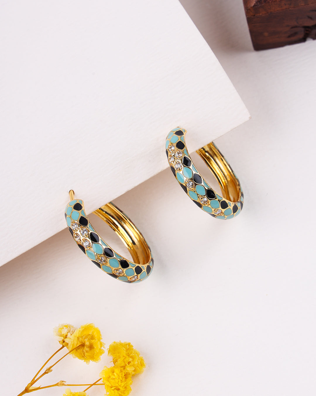 Gold hoop earrings with blue and black pattern on a white surface with yellow flowers.