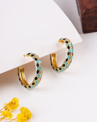 Gold hoop earrings with blue and black accents on a white surface with yellow flowers.