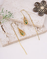Gold earrings with green gemstones on a textured stone surface