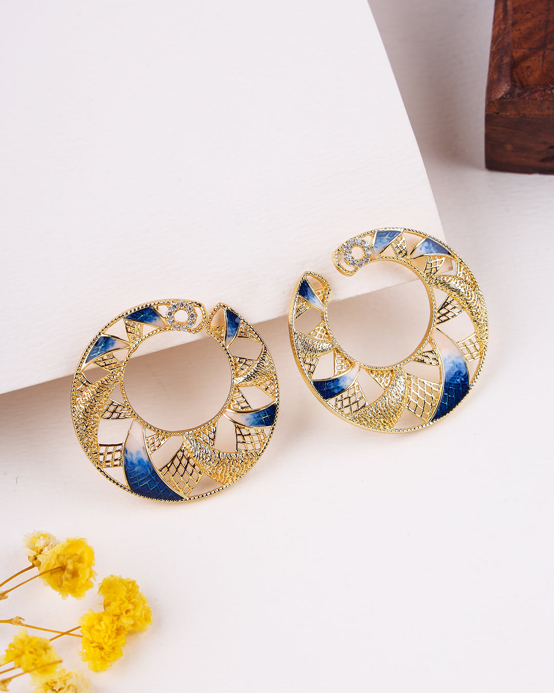 Gold and blue earrings on a white surface with yellow flowers.