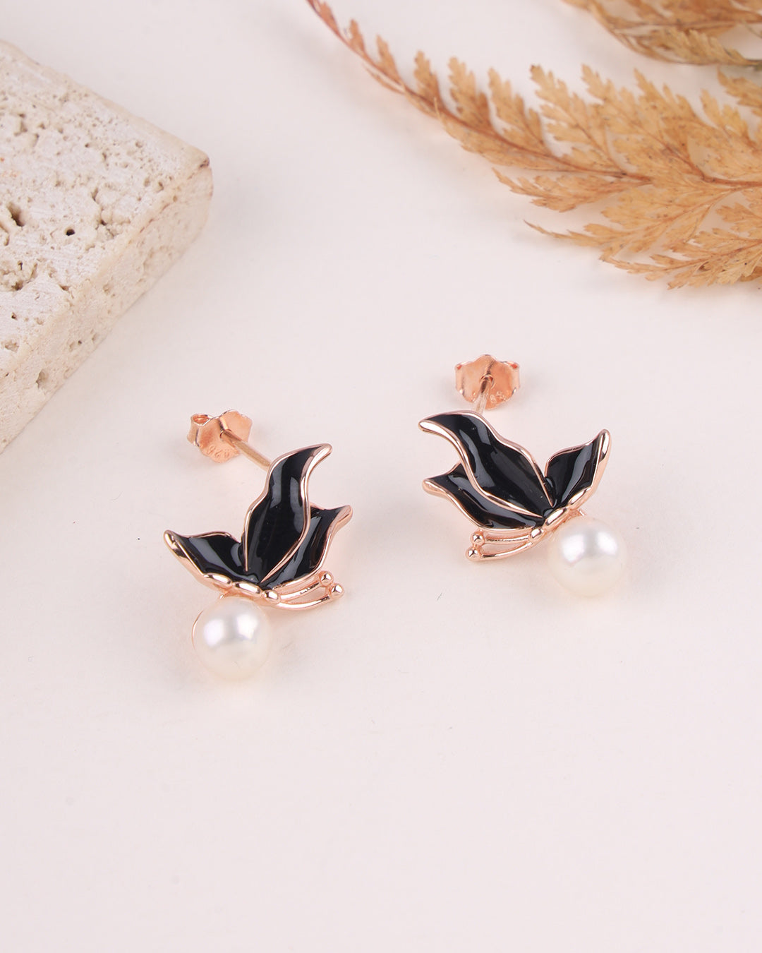 Pair of black and rose gold earrings on a light surface with dried plants.