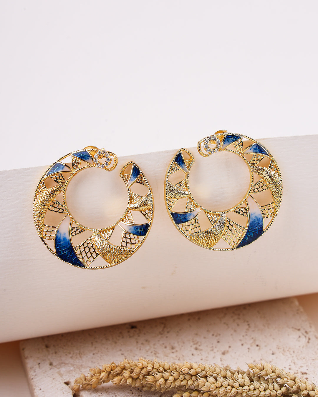 Gold and blue earrings on a white surface with a natural background